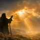 A prophet stands on a rocky hill at sunrise, raising his hands toward golden light breaking through clouds.