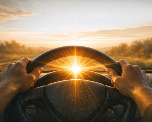 Silhouette of hands holding a steering wheel with sunlight shining