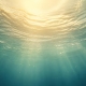 Underwater view looking up toward the rippled surface with sunlight streaming through the water.